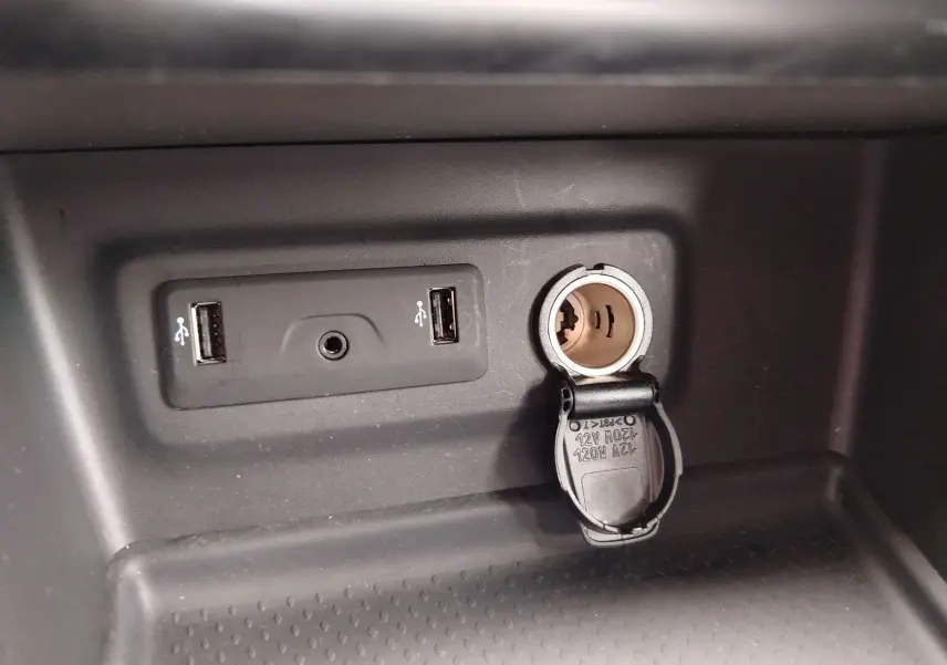 Gros plan sur la console centrale d’une Renault Mégane gris titanium 2018, montrant deux ports USB et une prise 12V ouverte.