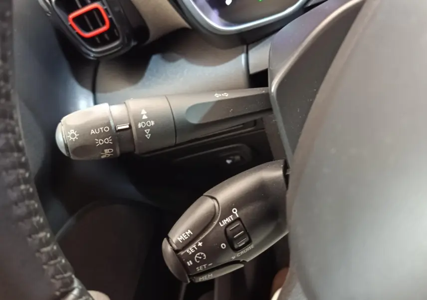Gros plan sur les commandes au volant côté gauche du Citroën C3 Aircross beige, avec réglages feux et régulateur de vitesse.