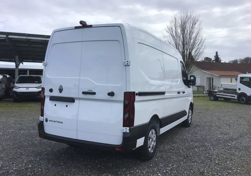 Vue 3/4 arrière droite d’un utilitaire Renault Master blanc avec portes arrière fermées sur un parking extérieur.