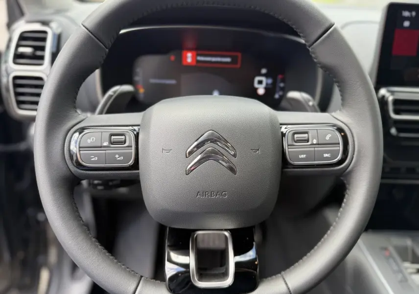 Vue rapprochée du volant en cuir noir du Citroën C5 Aircross 2025, avec commandes intégrées et logo chromé central.