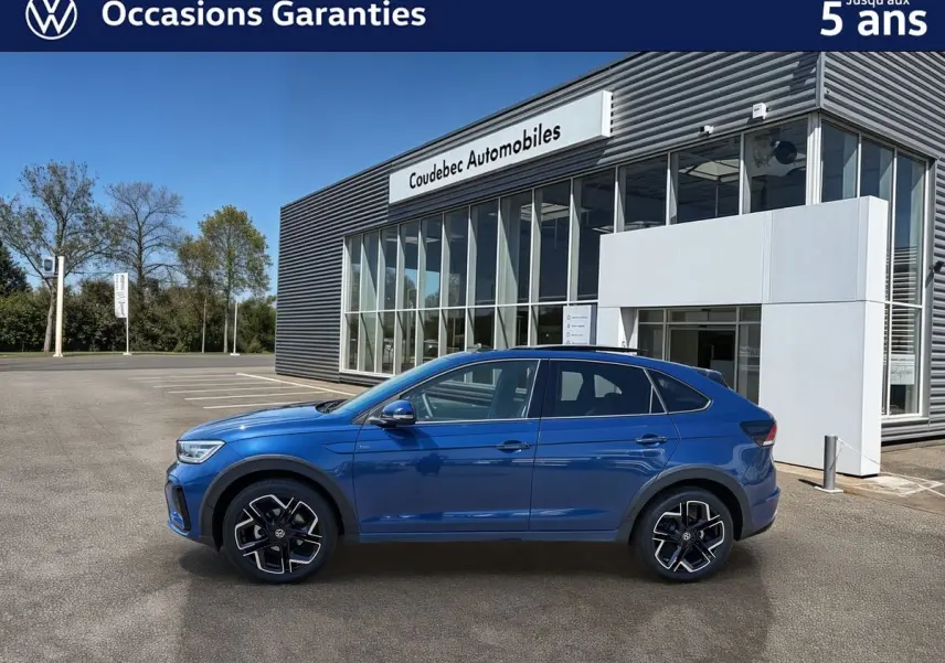 Profil côté gauche du Volkswagen Taigo bleu métallisé 2025, avec jantes alliage noires et toit ouvrant en verre.