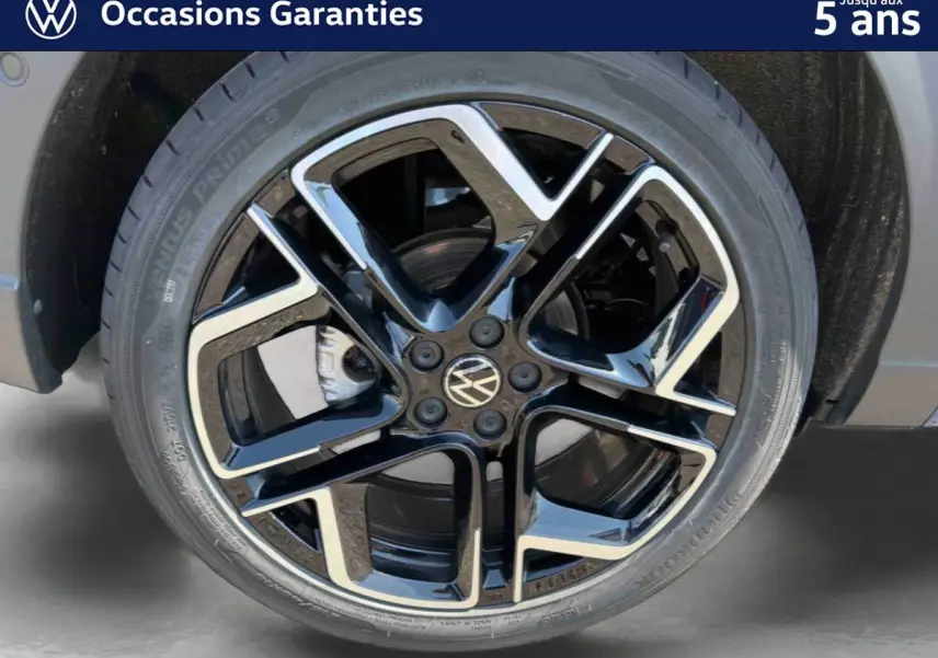 Gros plan sur la jante alliage noir et argent 18 pouces du Volkswagen Taigo bleu, avec logo VW central visible.