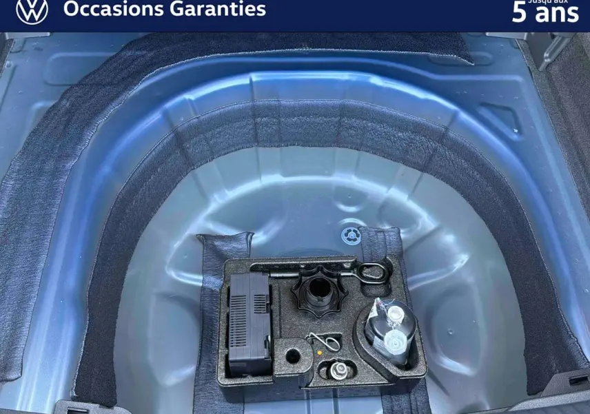 Vue plongeante sur le coffre ouvert d'un Volkswagen Taigo bleu, montrant la roue de secours et les outils de bord.