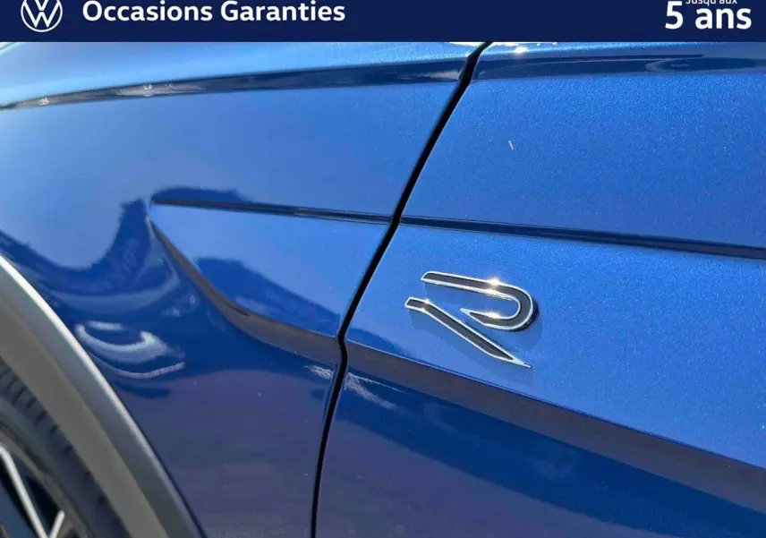 Détail du logo "R" sur l'aile avant droite d'un Volkswagen Taigo bleu métallisé sous lumière naturelle.