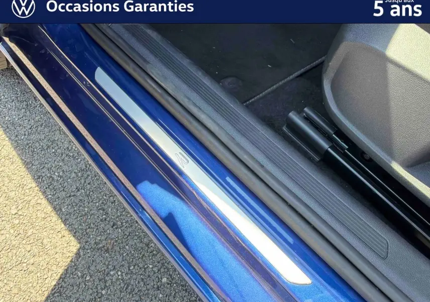 Gros plan sur la porte côté gauche d’un Volkswagen Taigo bleu métallisé avec seuil de porte en métal.