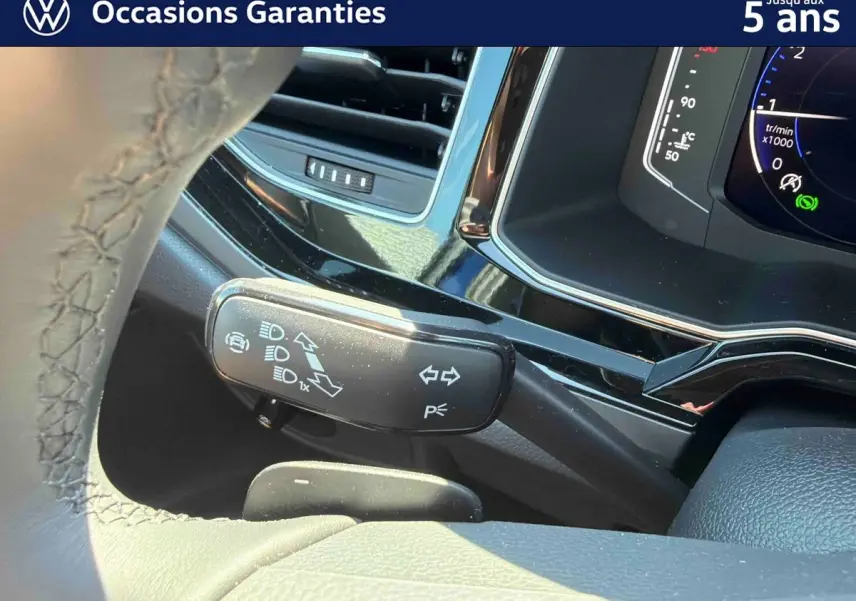 Gros plan sur la manette de clignotant à gauche du volant d’un Volkswagen Taigo bleu, tableau de bord digital visible.