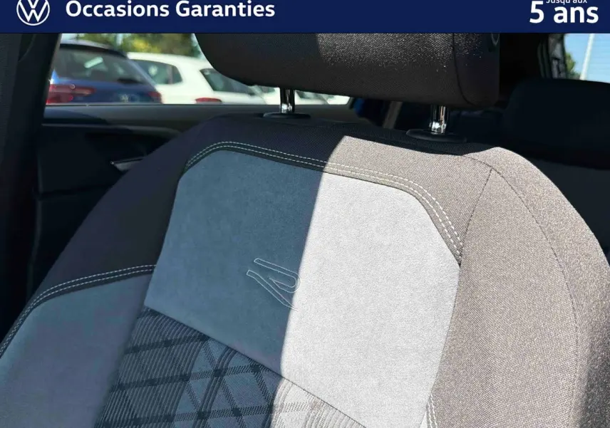 Détail du siège avant gris avec surpiqûres blanches et logo R embossé, intérieur du Volkswagen Taigo 2025.