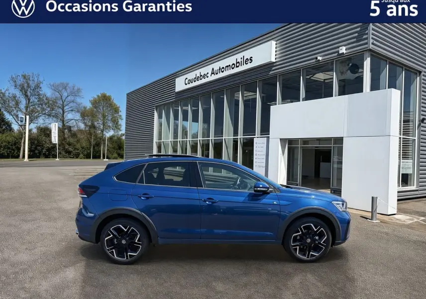 Profil côté gauche d'un Volkswagen Taigo bleu métallisé 2025 avec jantes alliage noires devant un bâtiment moderne.