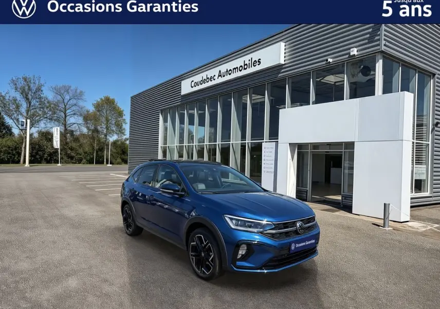 Vue 3/4 avant droite d'un Volkswagen Taigo bleu métallisé devant un showroom Coudebec Automobiles.