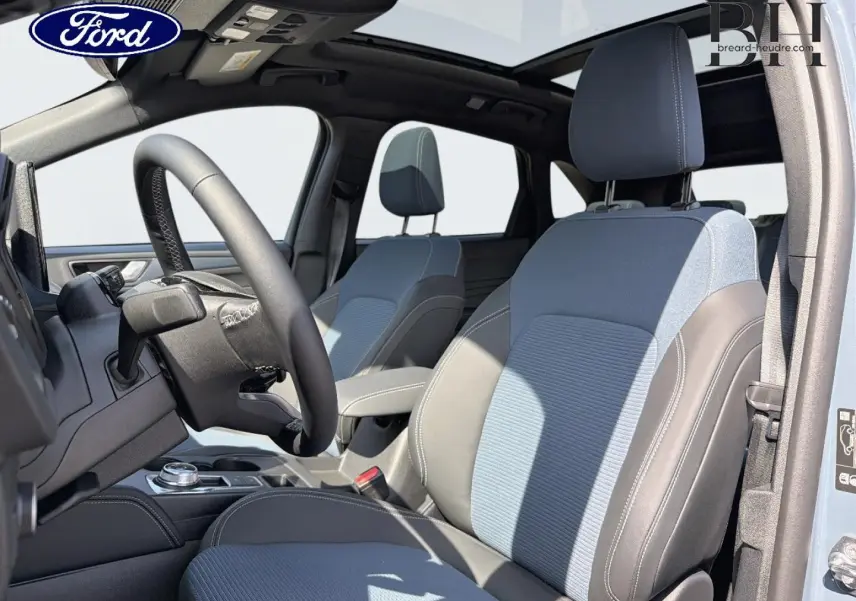 Vue intérieure côté conducteur du Ford Kuga 2026 bleu avec sièges bicolores et toit ouvrant panoramique.