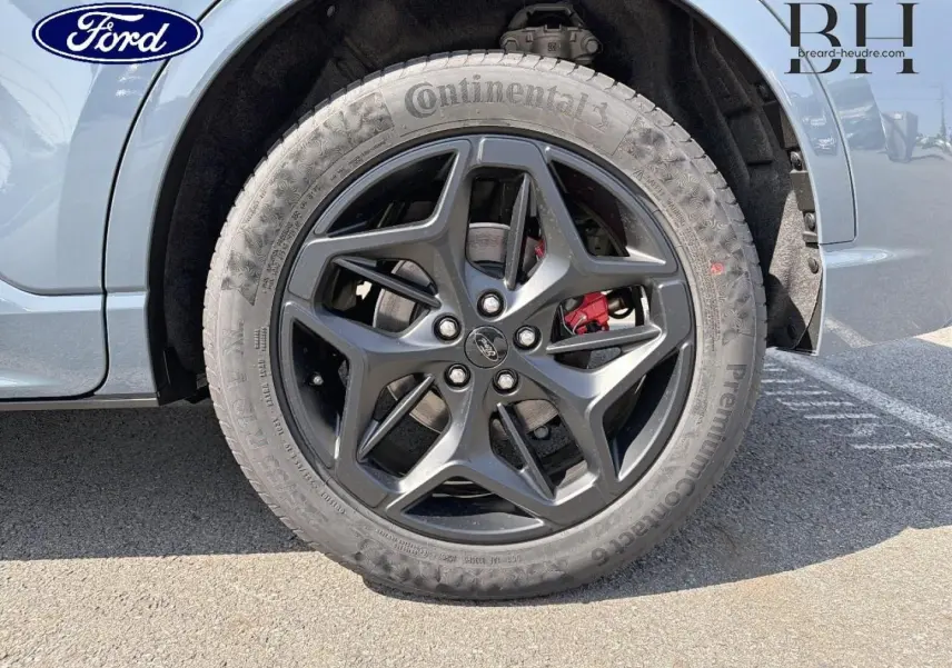 Gros plan sur la roue avant droite du Ford Kuga bleu, jante alliage noire avec étrier de frein rouge visible.