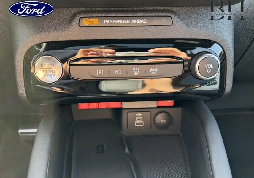Détail de la console centrale du Ford Kuga 2026 avec bouton start/stop, commandes clim et prises USB/12V en vue frontale rapprochée.