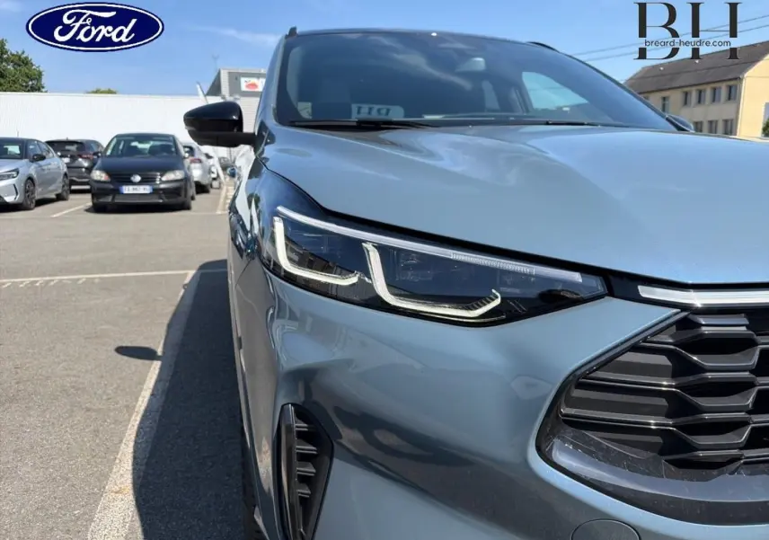 Gros plan sur l’avant droit du Ford Kuga bleu métallisé, mettant en valeur le phare LED et la calandre noire.