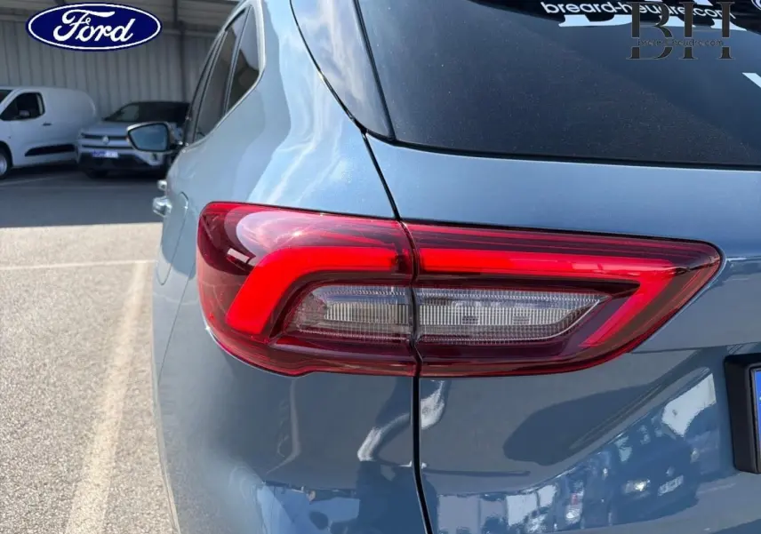 Feu arrière gauche en gros plan du Ford Kuga bleu, vue arrière côté gauche avec reflet sur la carrosserie.