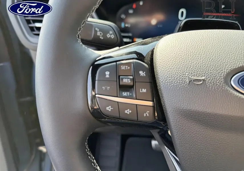 Gros plan sur le volant noir du Ford Kuga 2026 avec commandes multifonctions et logo Ford visible.
