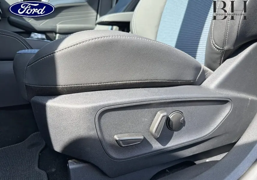 Gros plan sur les commandes de réglage électrique du siège conducteur gris du Ford Kuga 2026, intérieur lumineux.