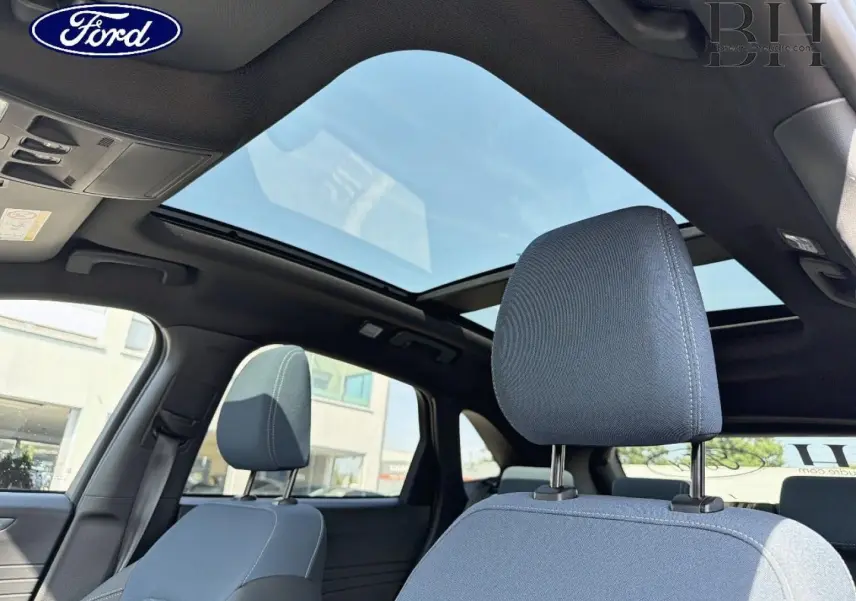 Vue intérieure du Ford Kuga 2026 montrant les sièges avant gris et le toit ouvrant panoramique en verre.