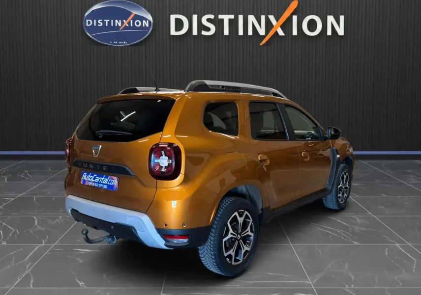 Vue 3/4 arrière droite d'un Dacia Duster orange 2020 avec attelage et jantes bi-ton dans un showroom.