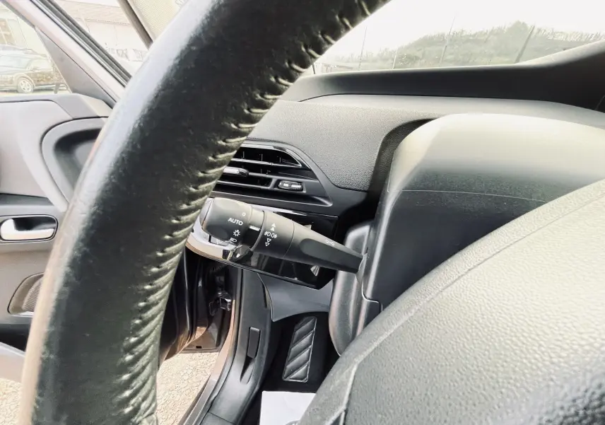 Gros plan sur la colonne de direction et le commodo d'éclairage à gauche du volant dans l'habitacle d'une Citroën C4 Picasso gris.