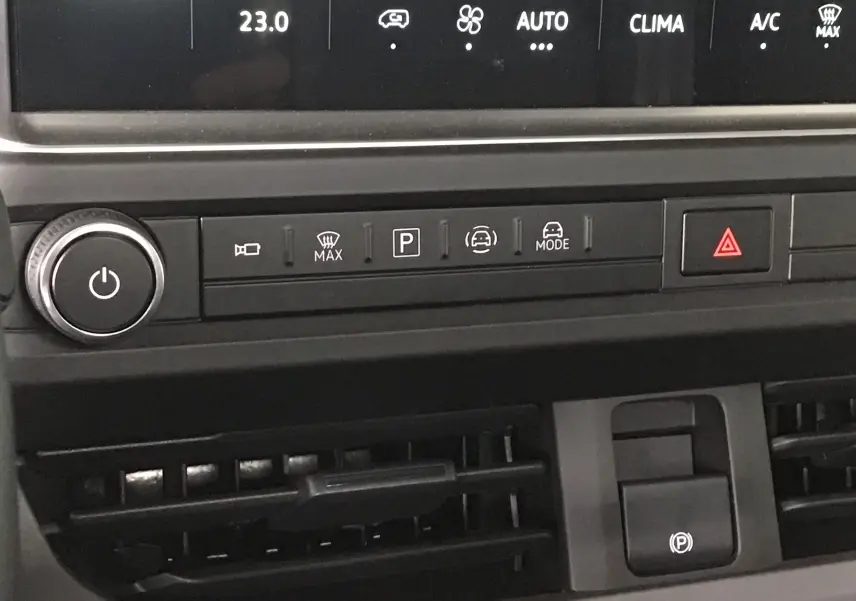 Gros plan sur la console centrale du Volkswagen Transporter T7, montrant les commandes de climatisation et le frein à main électrique.