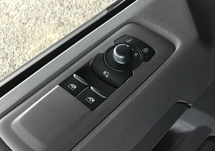 Commandes des rétroviseurs et vitres électriques sur la portière côté conducteur du Volkswagen Transporter T7 gris anthracite.