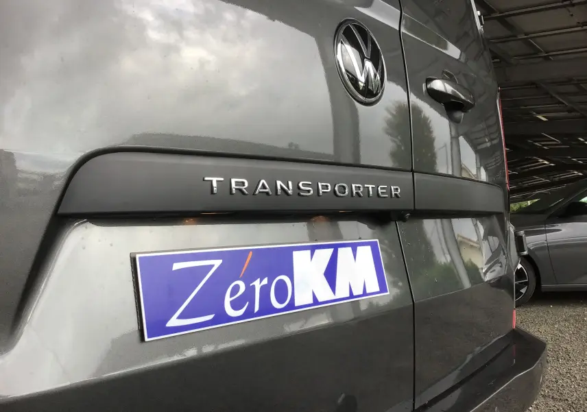 Vue rapprochée arrière droite du Volkswagen Transporter gris anthracite avec logo et plaque Zéro KM visible.