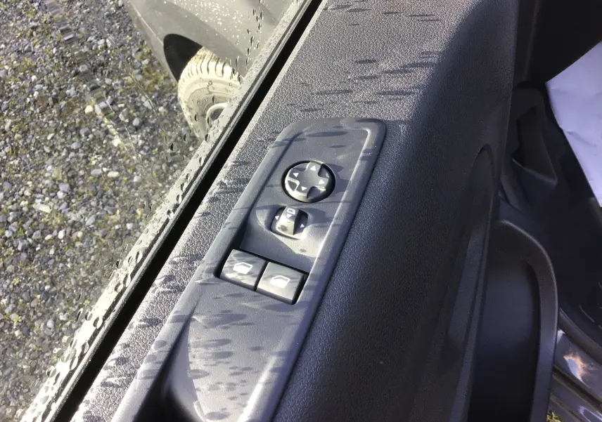 Gros plan sur les commandes de réglage des rétroviseurs et vitres côté conducteur du Citroën Jumpy gris titane, porte ouverte.
