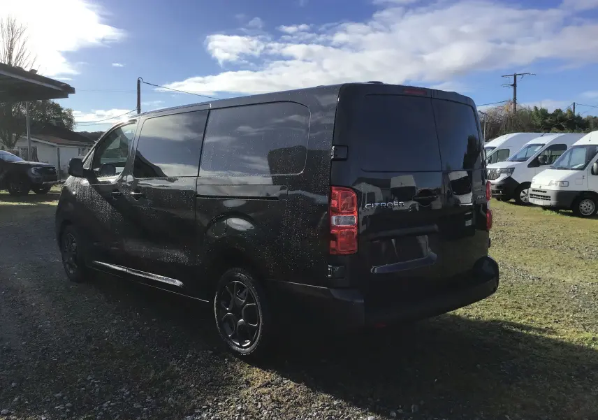 Vue 3/4 arrière droite d'un Citroën Jumpy XL gris titane avec vitres teintées et jantes noires sur un parking extérieur.