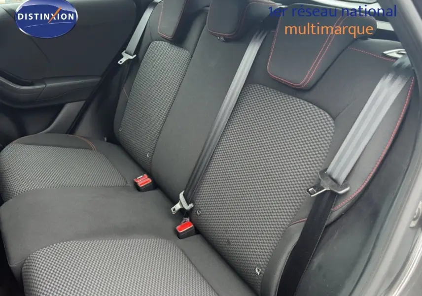 Vue intérieure sur les sièges arrière en tissu noir à motifs gris avec surpiqûres rouges, porte ouverte côté droit.