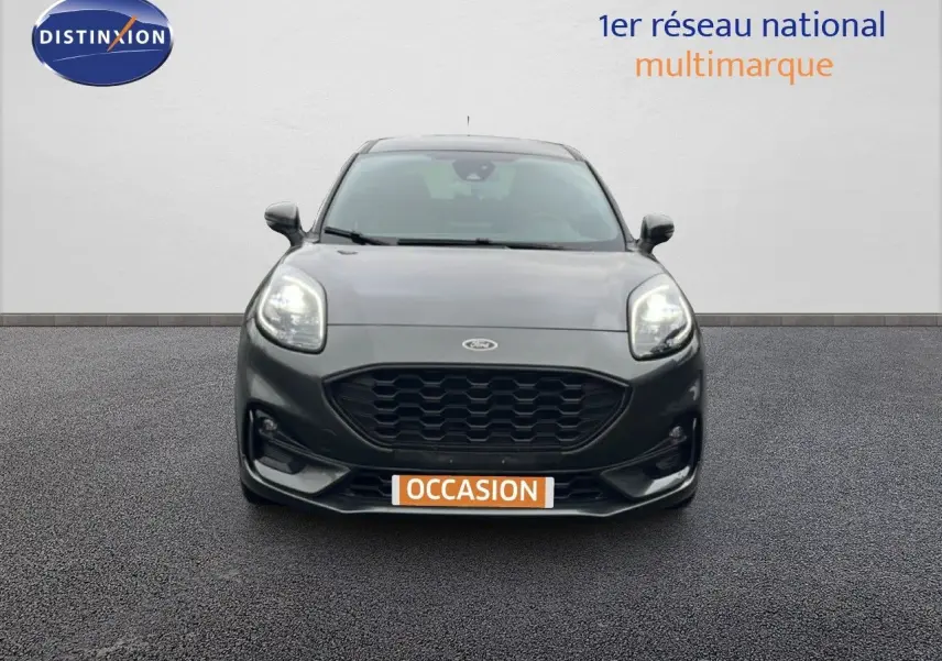 Vue frontale d'un Ford Puma gris magnetic metal 2024 avec calandre noire et phares allumés sur fond neutre.
