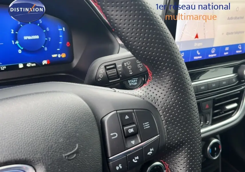 Vue rapprochée du volant perforé avec surpiqûres rouges et tableau de bord numérique du Ford Puma gris Magnetic Metal 2024.