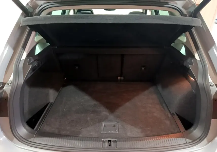 Coffre ouvert d’un Volkswagen Tiguan gris foncé, vue arrière montrant l’espace de chargement vide et la tablette relevée.