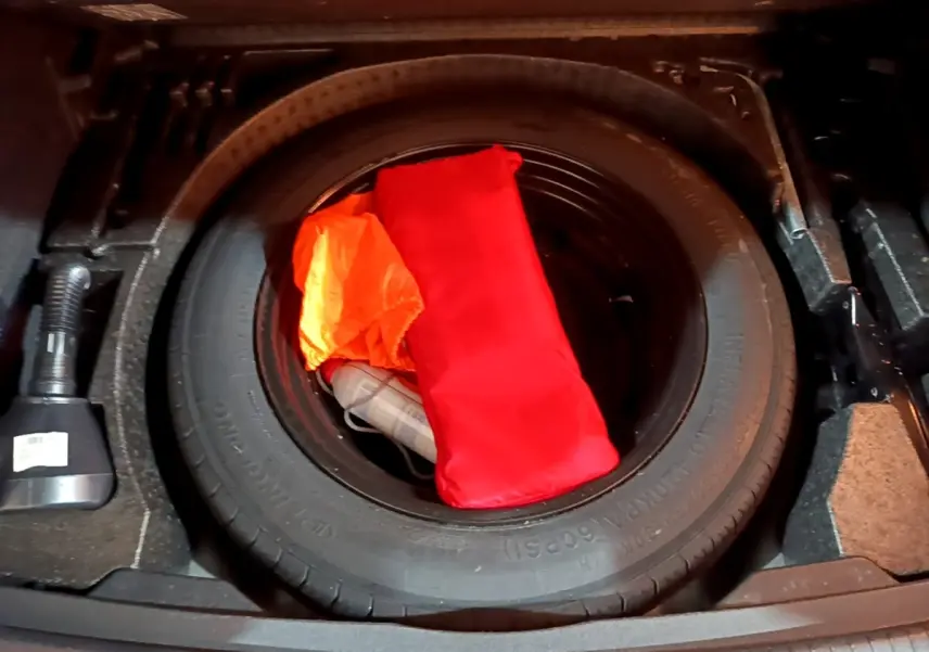 Gros plan sur la roue de secours dans le coffre d'un Volkswagen Tiguan 2021, avec trousse de secours rouge et gilet orange.