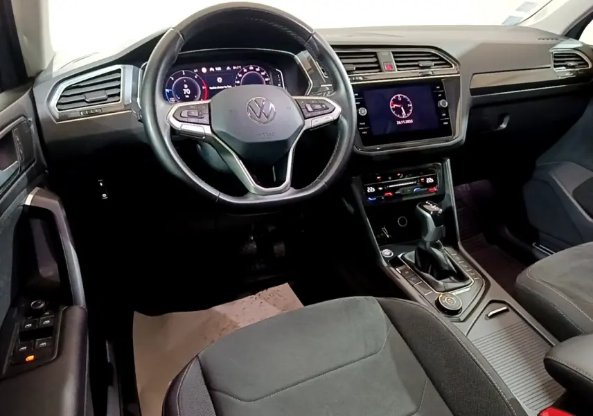 Intérieur avant du Volkswagen Tiguan gris foncé, volant cuir multifonctions et écran tactile central allumé.