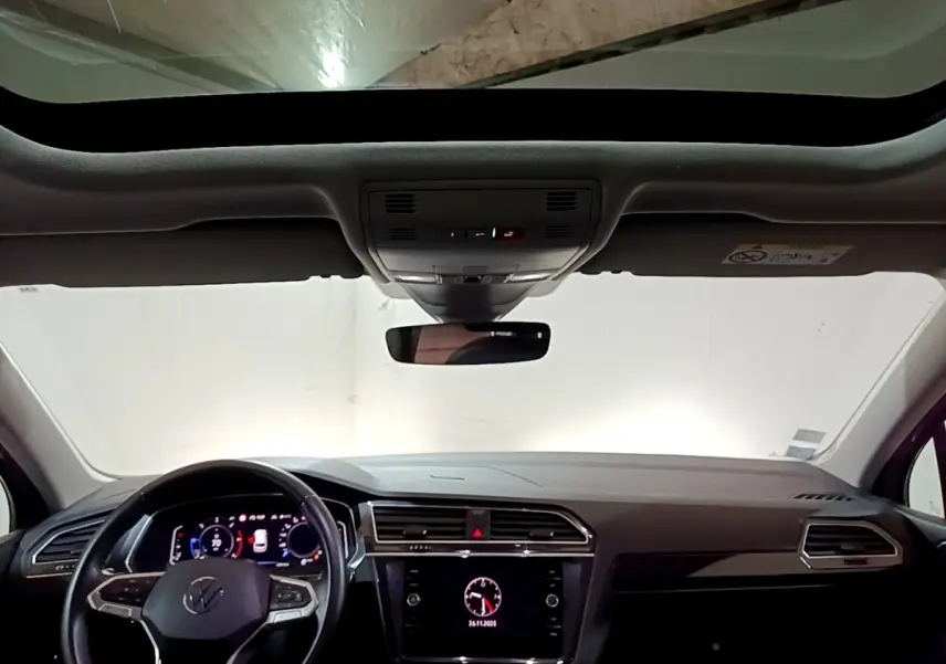 Vue intérieure avant du Volkswagen Tiguan 2.0 TDI gris foncé, tableau de bord moderne avec écran tactile et toit ouvrant panoramique.