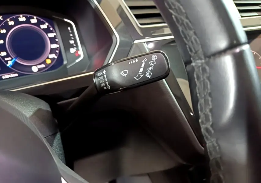 Gros plan sur la manette d'essuie-glace à gauche du volant cuir noir du Volkswagen Tiguan gris foncé, tableau de bord numérique visible.