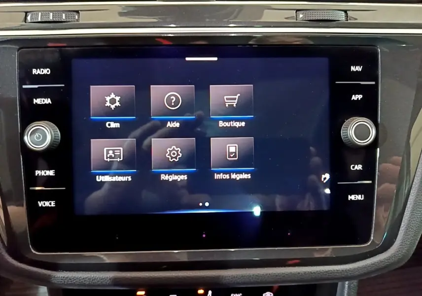 Écran tactile central du Volkswagen Tiguan 2021 affichant les menus climatisation, aide et boutique, entouré de commandes noires.