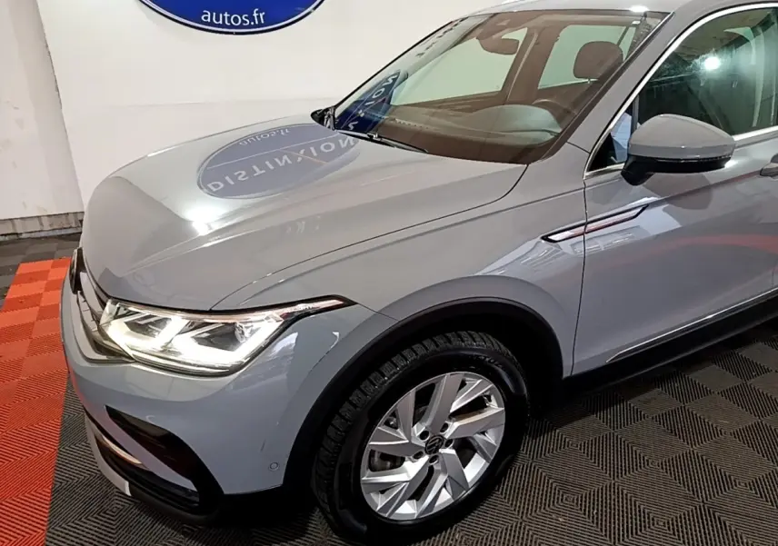 Vue 3/4 avant droit d'un Volkswagen Tiguan gris foncé avec phares LED allumés et jantes alliage visibles.