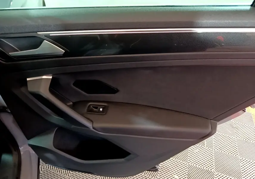 Vue intérieure de la porte côté droit du Volkswagen Tiguan gris foncé, avec poignée et bouton de verrouillage intégrés.
