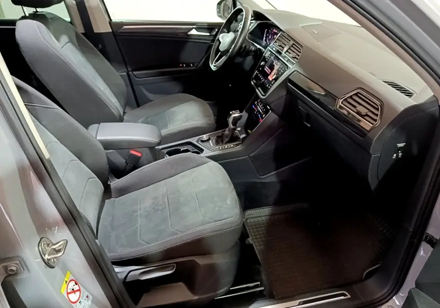 Intérieur avant du Volkswagen Tiguan gris foncé, montrant sièges tissu, volant cuir multifonctions et écran tactile central.