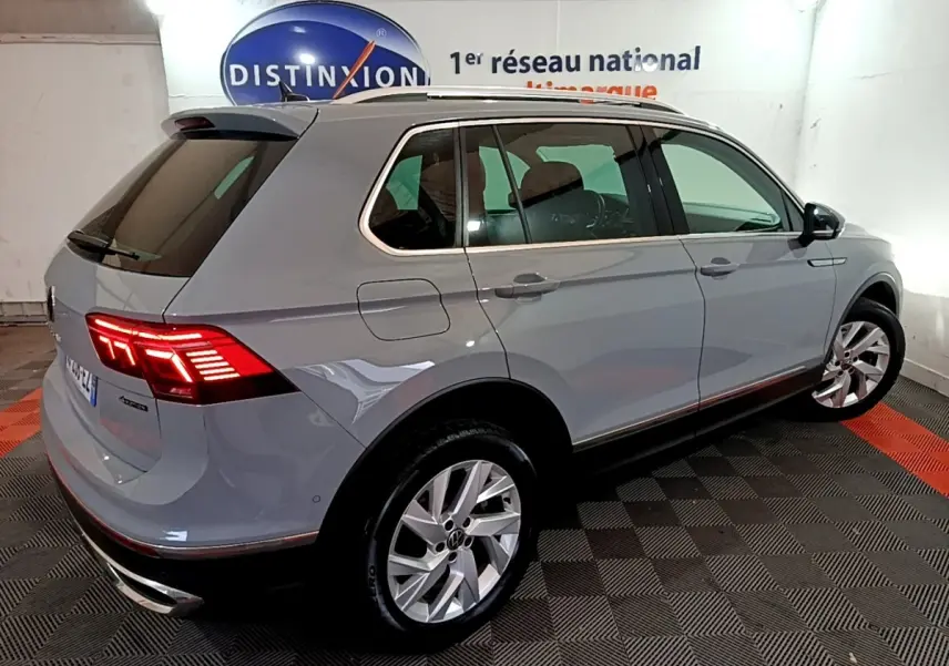 Volkswagen Tiguan gris foncé vu 3/4 arrière droit avec feux LED allumés dans un showroom intérieur.