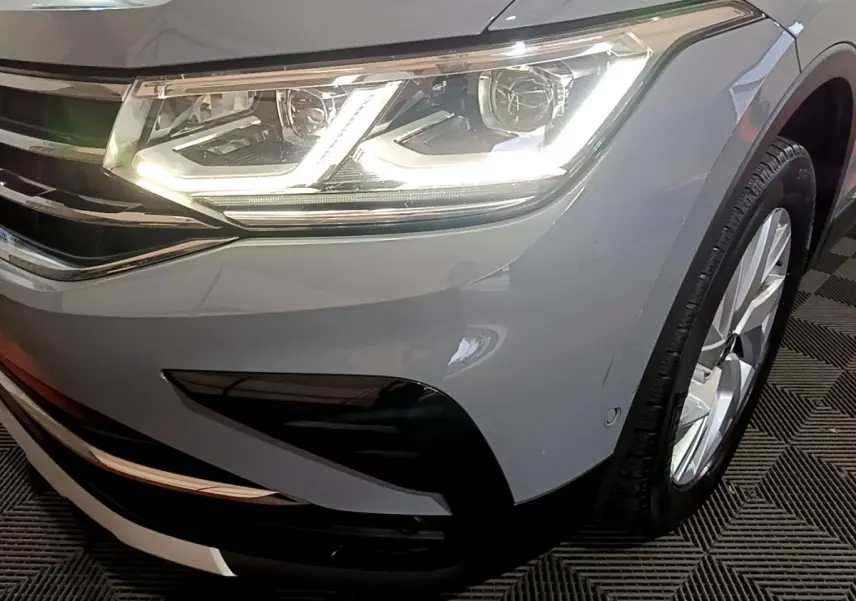 Gros plan sur l'avant droit gris foncé du Volkswagen Tiguan 2021, mettant en valeur le phare LED allumé et la roue.