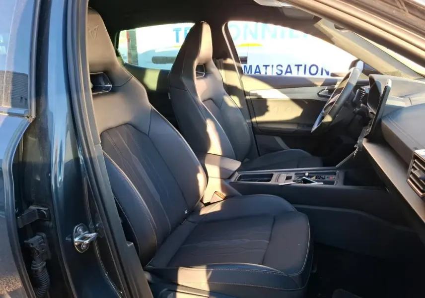 Vue intérieure côté conducteur du CUPRA Formentor gris foncé 2023, mettant en valeur les sièges sport en tissu noir avec surpiqûres contrastées.