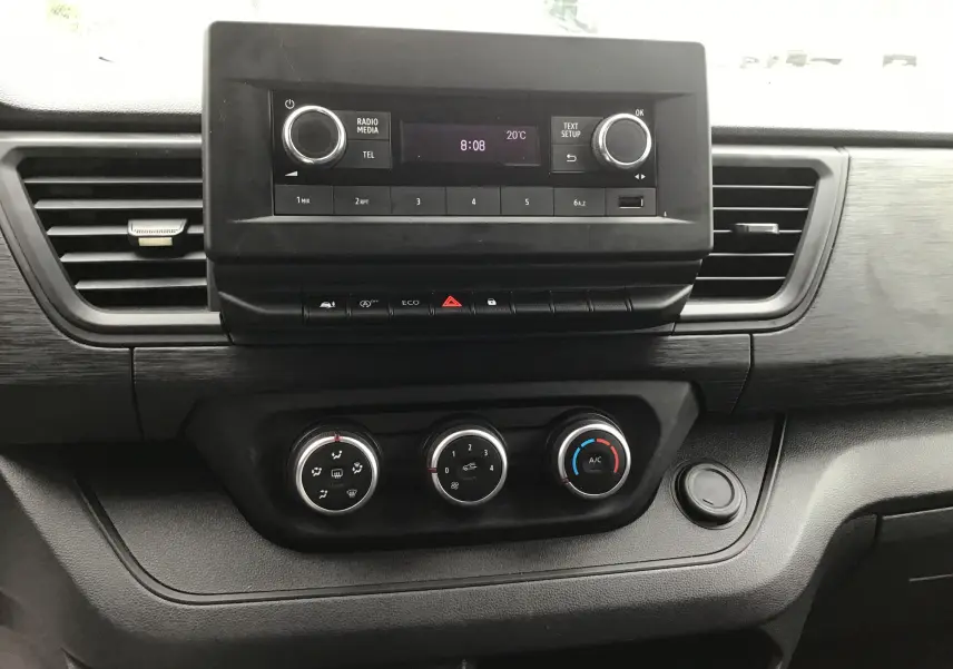 Vue rapprochée du tableau de bord noir avec radio et commandes de climatisation du Renault Trafic Fourgon blanc 2024.