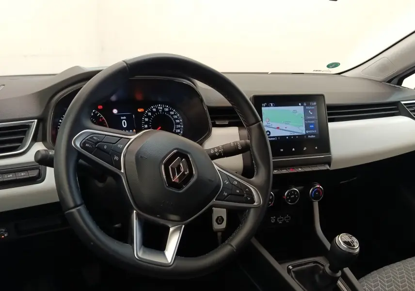 Vue intérieure de face du tableau de bord de la Renault Clio blanche, volant cuir et écran tactile central allumé.