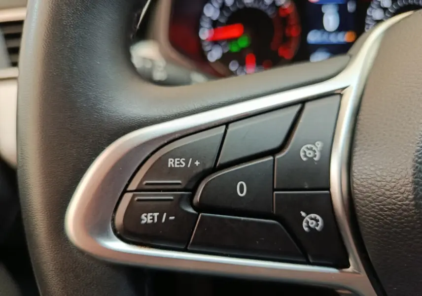 Gros plan sur les commandes du régulateur de vitesse au volant cuir synthétique d'une Renault Clio blanche 2023.