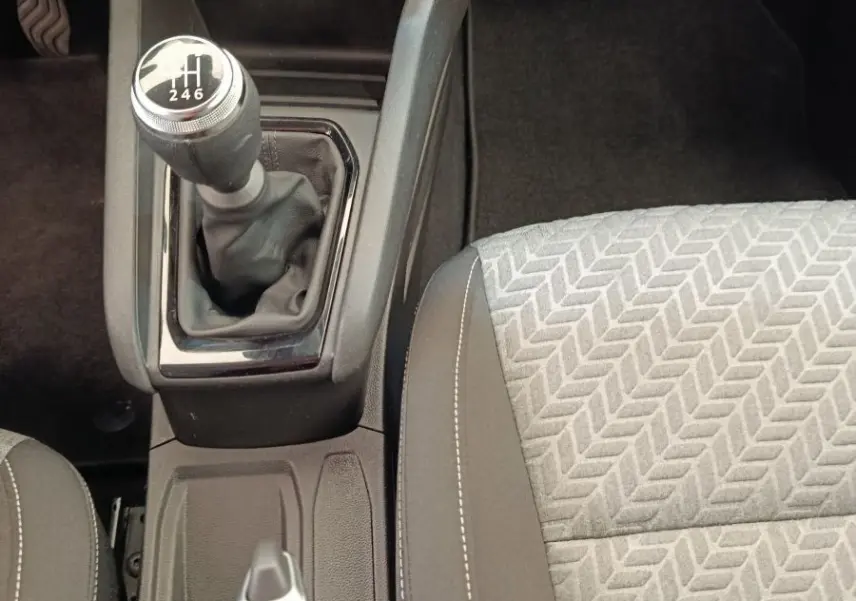 Vue plongeante sur la console centrale de la Renault Clio blanche 2023, avec levier de vitesses manuel et siège tissu gris à motifs.