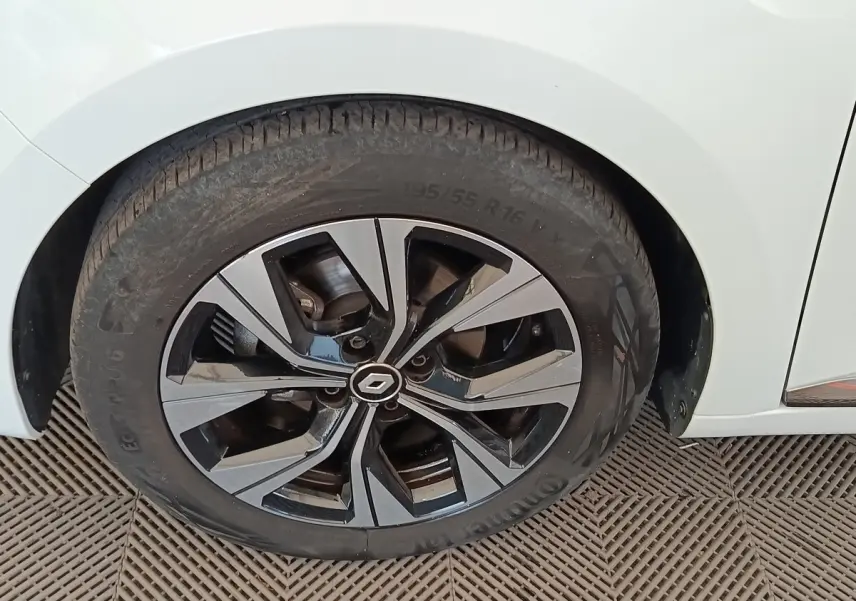 Gros plan sur la roue avant gauche d'une Renault Clio blanche, avec jante alliage bicolore et logo Renault central.