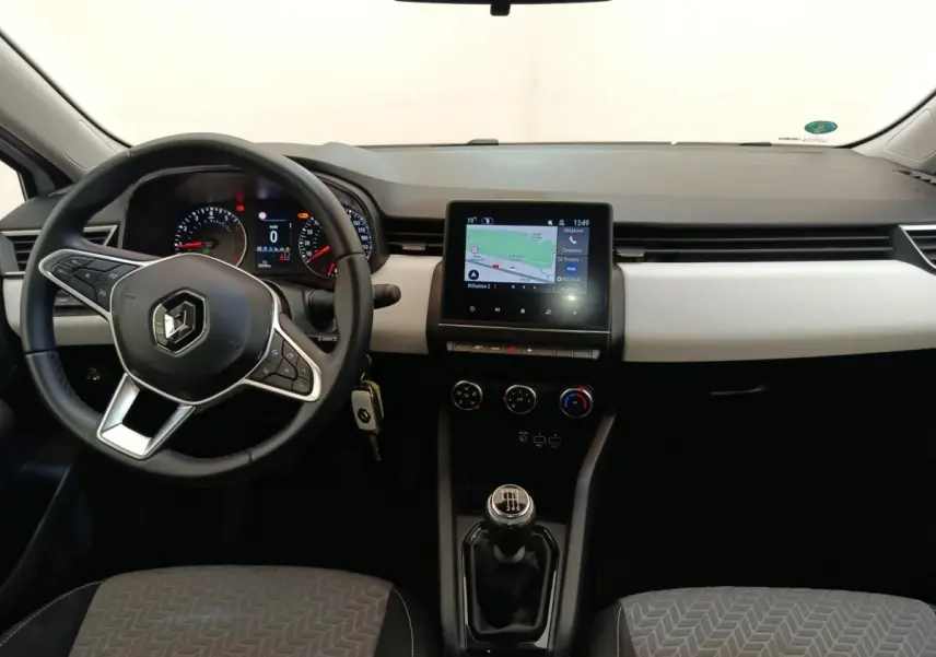 Vue intérieure avant de la Renault Clio blanche 2023 avec volant multifonctions, écran tactile central et boîte manuelle.
