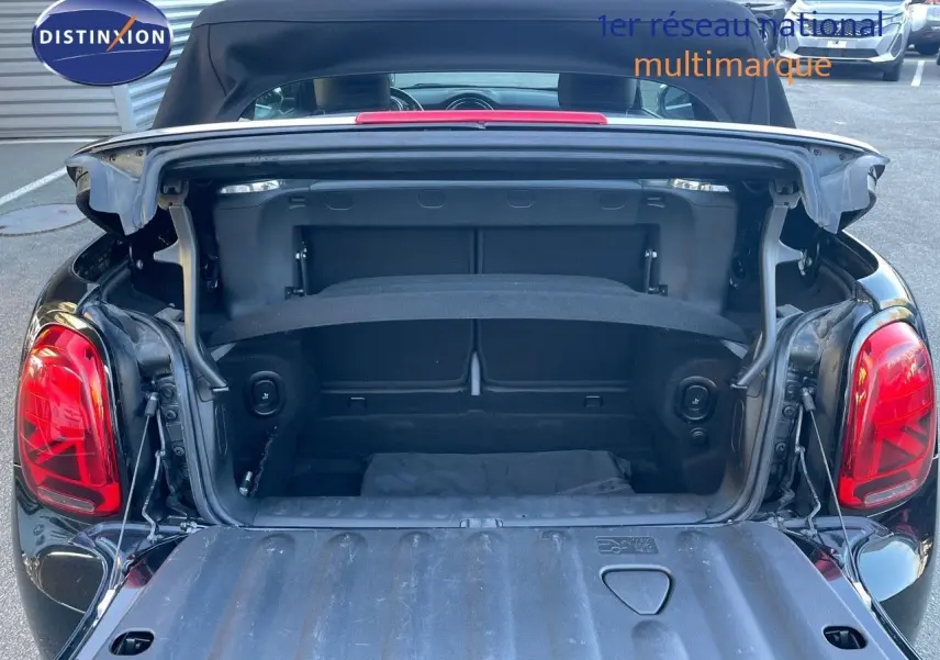 Coffre ouvert vu de l'arrière d'une MINI Cabriolet F57 noire Midnight Metal avec capote relevée sur parking.